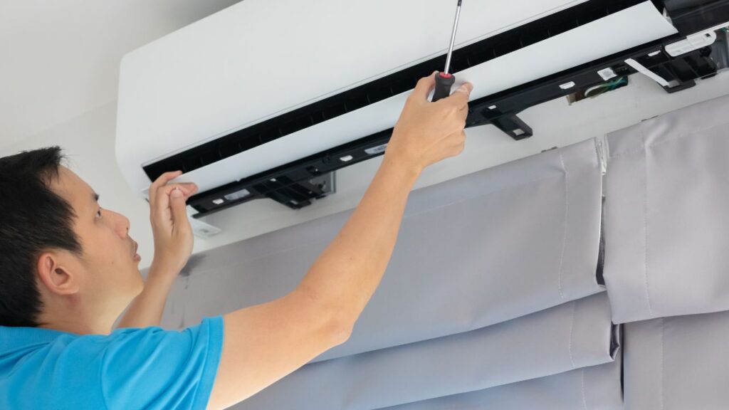 Maintenance technician repairing a wall-mounted air conditioning unit in a rental home