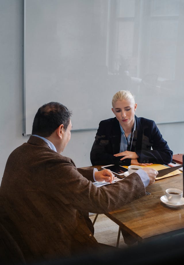Two professionals discussing paperwork at a table with coffee cups in an office setting.